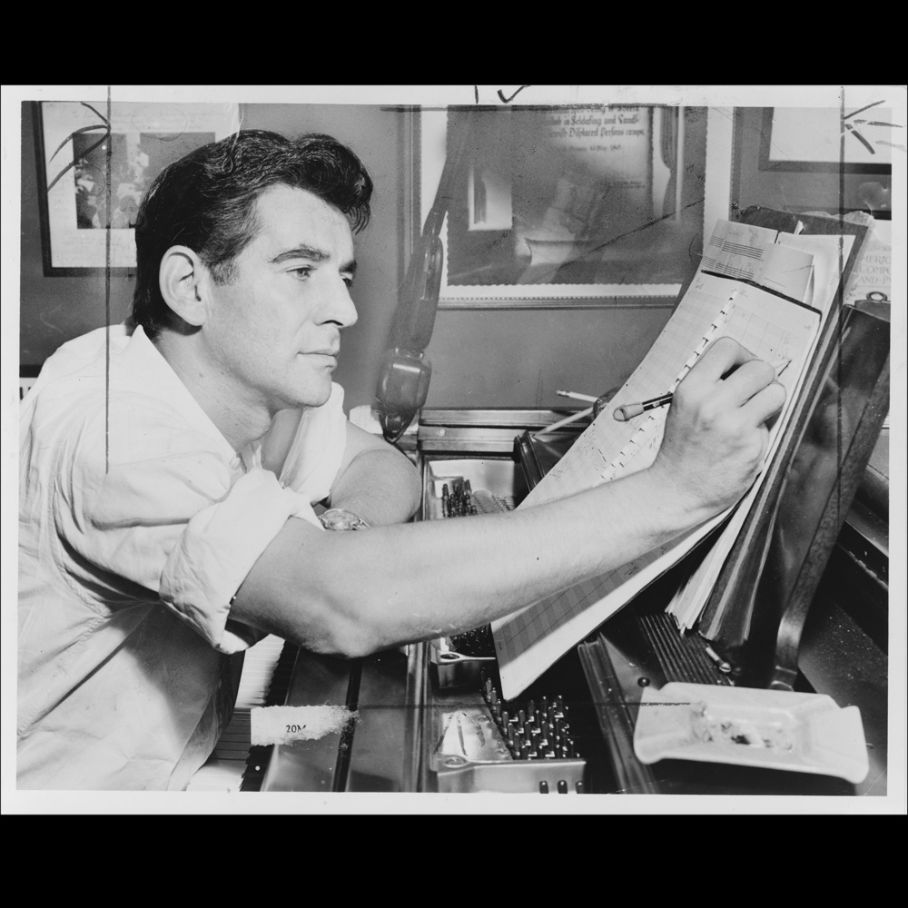 Leonard Bernstein, half-length portrait, facing right, seated at piano, making annotations to musical score